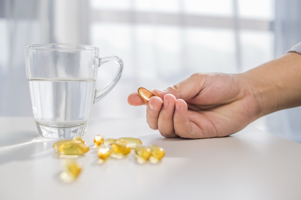 healthy lifestyle, medicine, nutritional supplements and people concept - close up of male hands holding pills with cod liver oil capsules and water glass