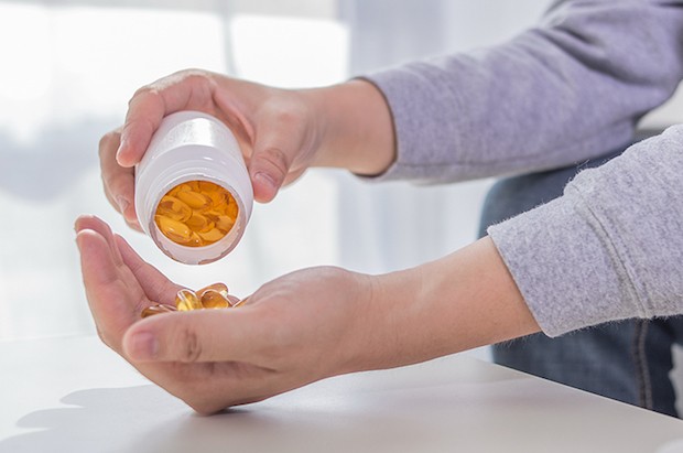 healthy lifestyle, medicine, nutritional supplements and people concept - close up of male hands holding pills with cod liver oil capsules and water glass